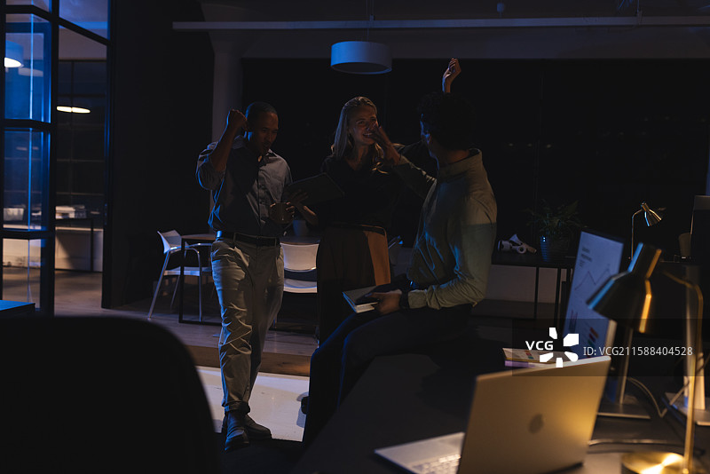 庆祝成功，同事们在现代办公室里深夜工作时击掌庆祝图片素材