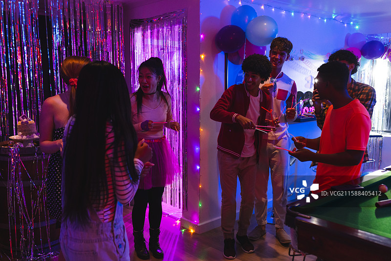 青少年在室内享受热闹的生日派对，蛋糕和五彩缤纷的装饰品环绕着他们。图片素材