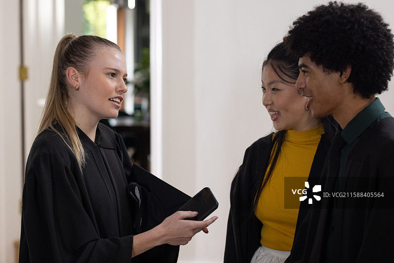 穿着学位袍的青少年们在一起交谈和微笑，共同庆祝学校的成就。图片素材