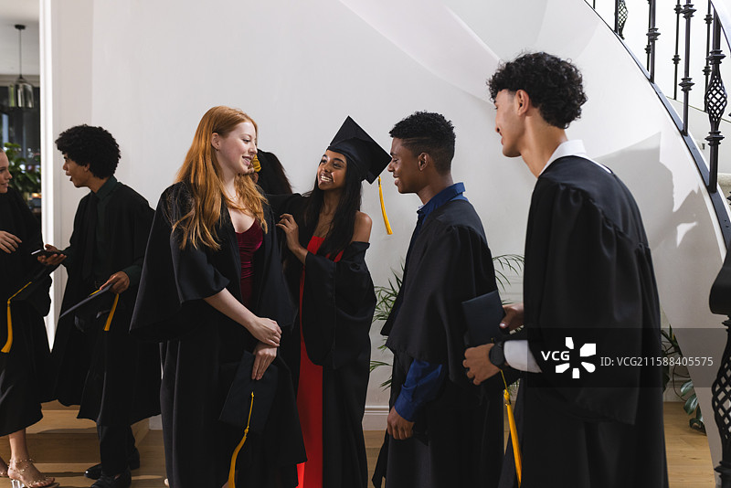 穿着毕业袍的青少年们在室内欢庆，微笑聊天。图片素材