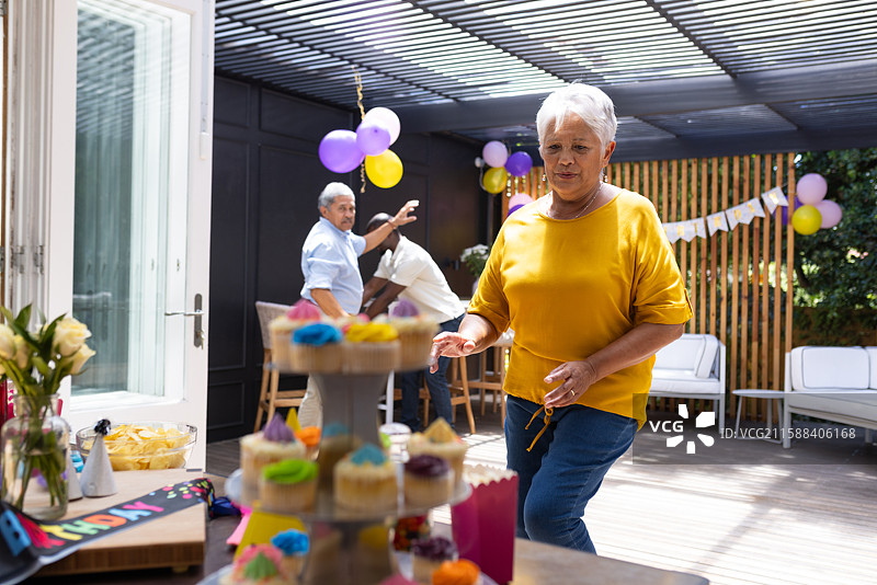 祖母在阳光明媚的露台上享受五彩缤纷的杯子蛋糕，庆祝家庭生日派对。图片素材