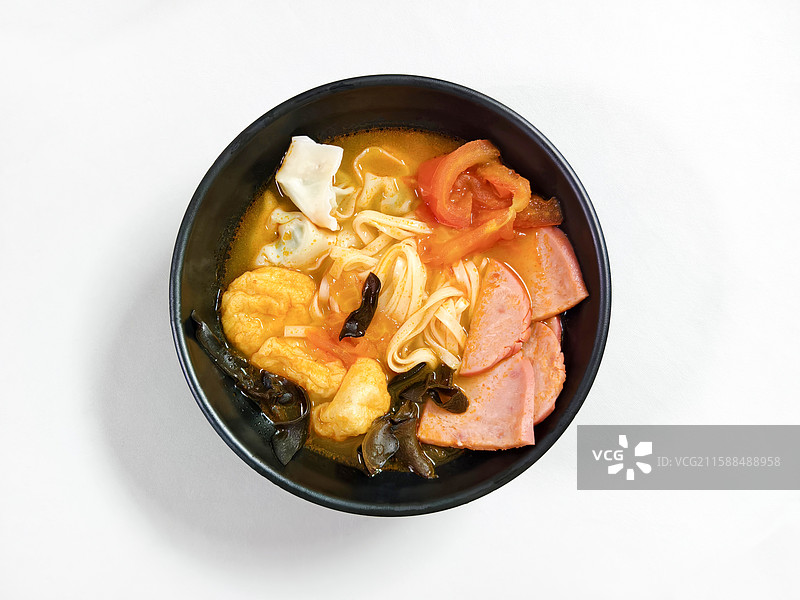一碗配料丰富的全家福火腿面，有西红柿、火腿、木耳、福袋、豆腐、小馄饨等，纯色背景图片素材
