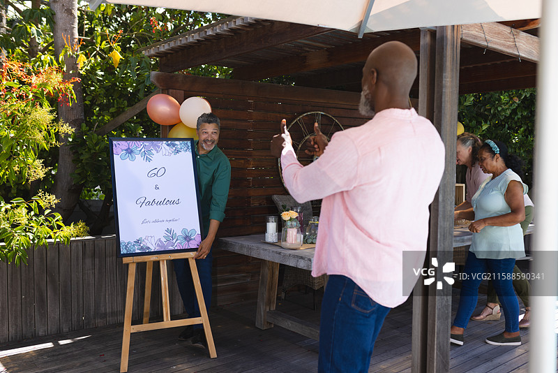 庆祝60岁生日的非裔美国男性正在为朋友拍照，朋友手持标志。图片素材