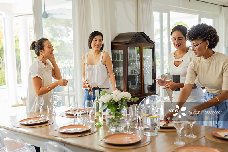 布置优雅的餐桌，摆放玻璃器皿和鲜花，女性正在准备庆祝活动图片素材