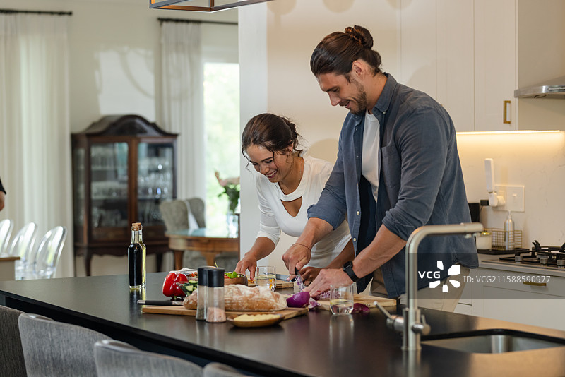 一对情侣在现代厨房里一起准备餐点，微笑着享受烹饪的乐趣图片素材