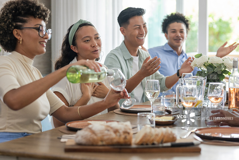 倒酒，朋友们在餐桌旁欢笑，桌上有面包和鲜花图片素材