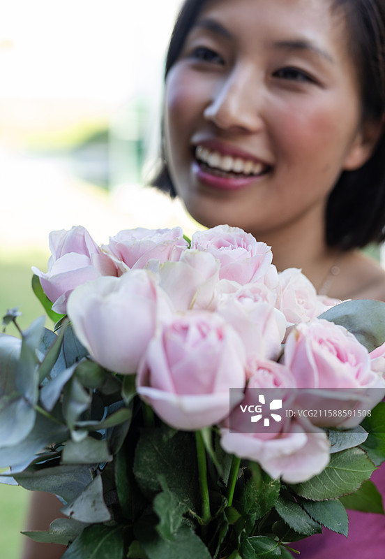 微笑的女性手捧粉色玫瑰花束，在户外庆祝快乐的婚礼时刻图片素材