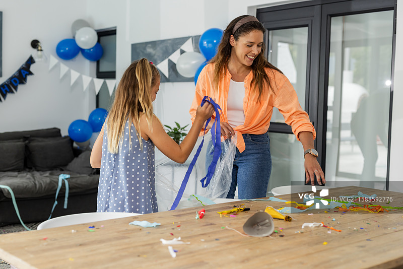 母亲和女儿在家中清理生日派对后的杂物，开心地在一起微笑。图片素材