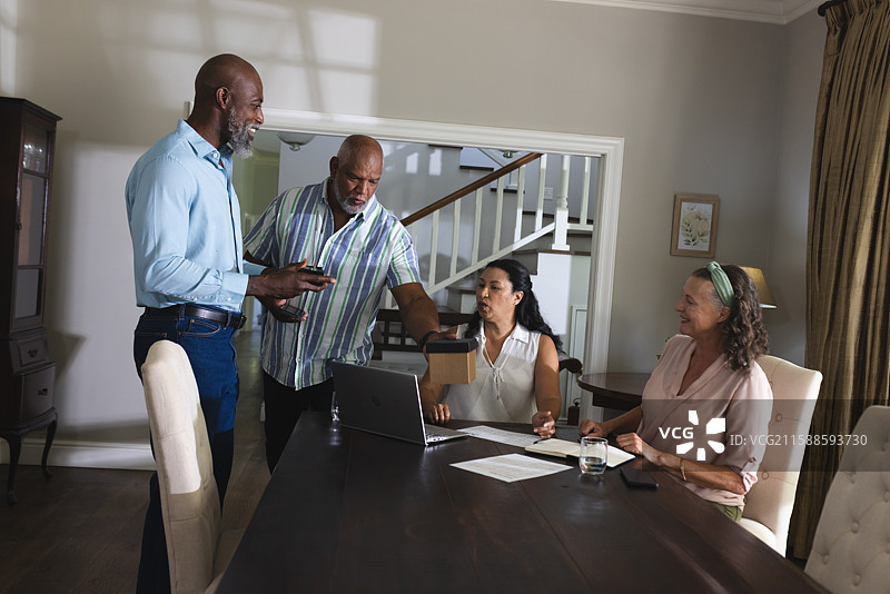 老年人在家中围坐在桌子旁讨论项目，桌上有笔记本电脑和文件。图片素材