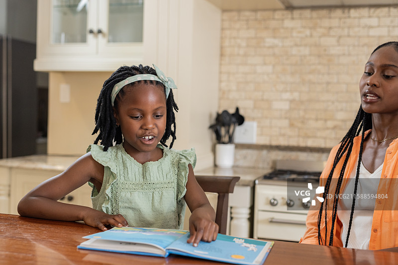 小女孩在厨房桌子上和妈妈一起阅读书籍，享受美好时光图片素材