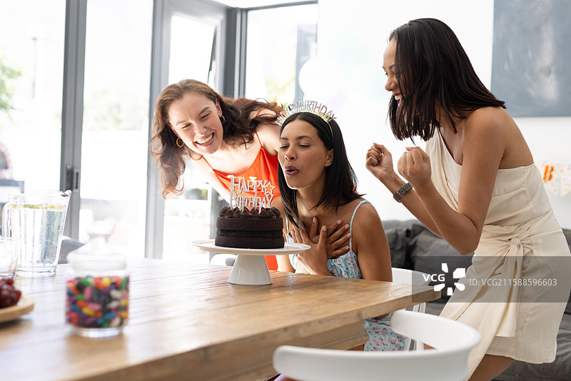 年轻女性在室内庆祝生日，吹灭巧克力蛋糕上的蜡烛图片素材