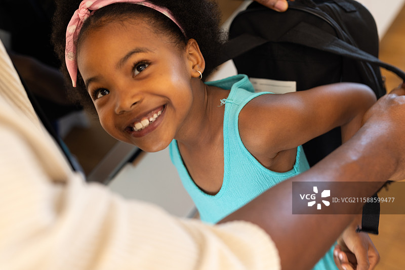 微笑的女孩背着书包，在父母的帮助下准备上学图片素材