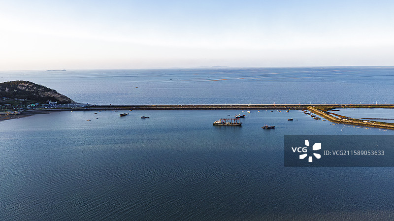 连云港港湾碧波荡漾，栈桥蜿蜒入海，船只静泊于蓝天白云之下。远山与城市轮廓相映，完美融合工业活力。图片素材