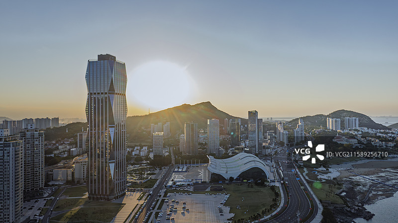 连云区海滨大道，现代建筑与自然山海完美融合。金色余晖洒在公路、沙滩与海面上，展现港口城市繁荣与宁静。图片素材