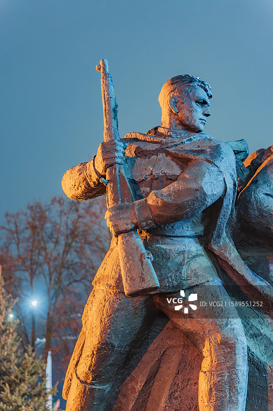暮色中，手持步枪的苏联士兵纪念雕像被橙色与蓝色光线照亮图片素材
