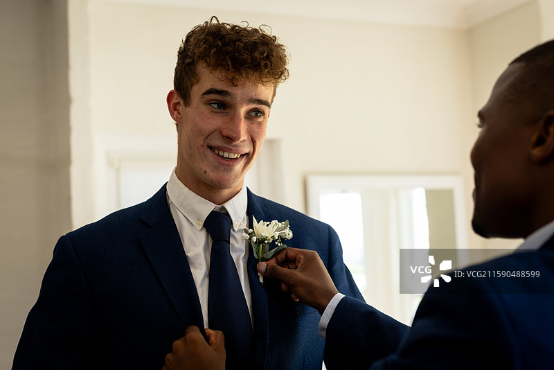 新郎微笑着，朋友为他调整胸花，准备婚礼仪式。图片素材