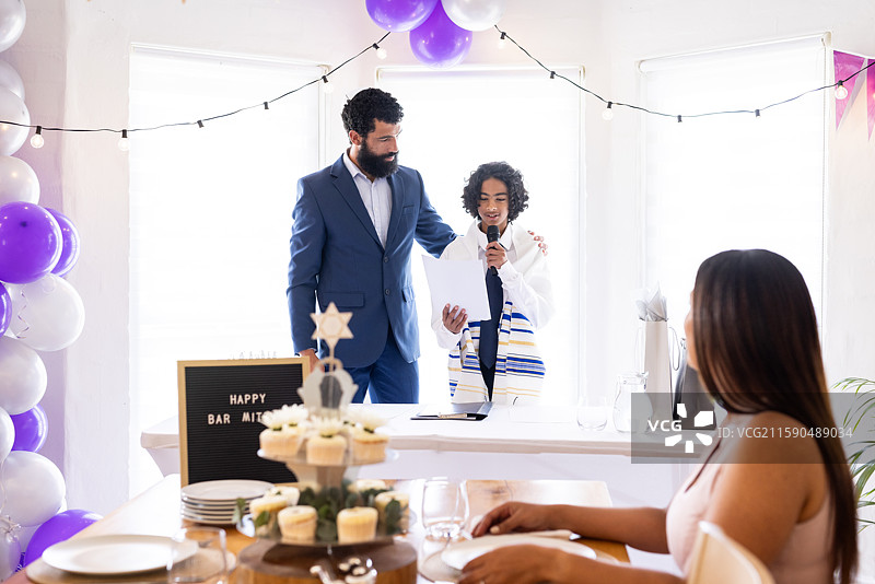 庆祝男孩的巴尔米茨瓦，男孩对着麦克风讲话，身边有家人和装饰品图片素材