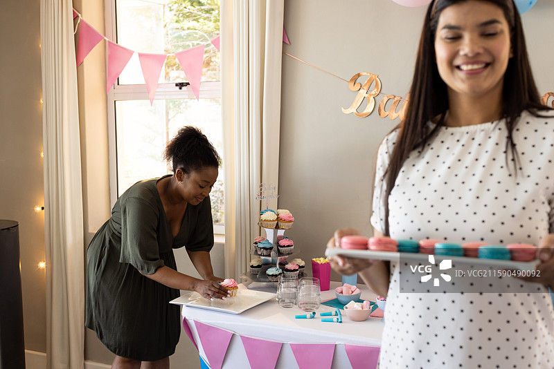 女性为庆祝婴儿洗礼派对准备五彩缤纷的马卡龙和杯子蛋糕图片素材