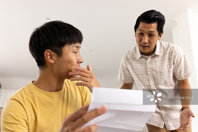 父亲在家中与儿子讨论重要文件，两人看起来都很沉思。图片素材