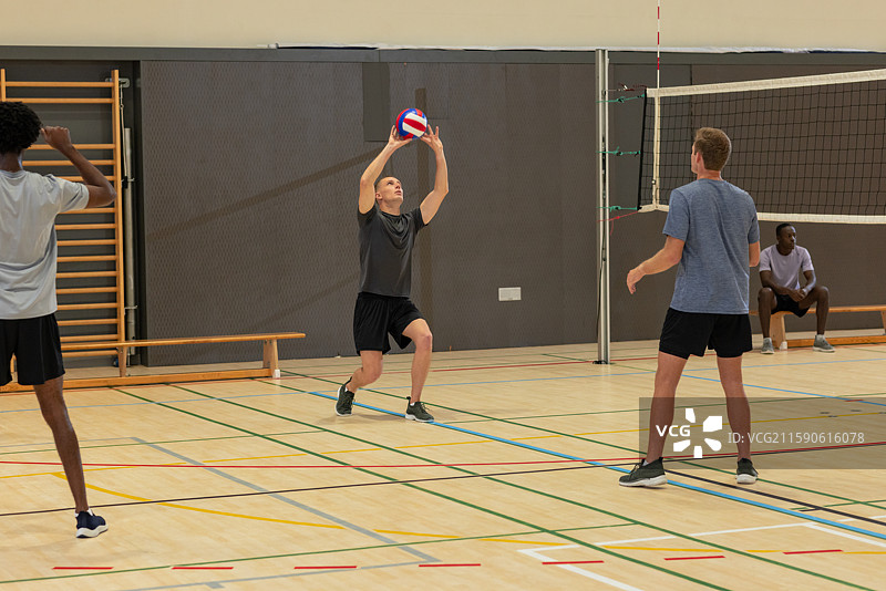 多样化的男性排球搭档穿着运动服在学校体育馆的排球网上热身图片素材