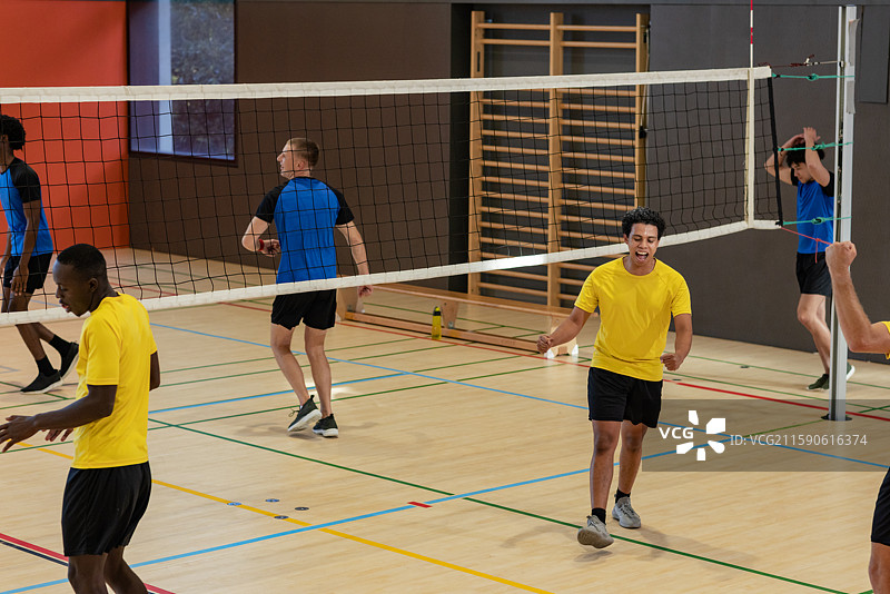 穿着运动衫的男子在健身房庆祝得分，背景有网格标记、墙杆和水瓶。图片素材