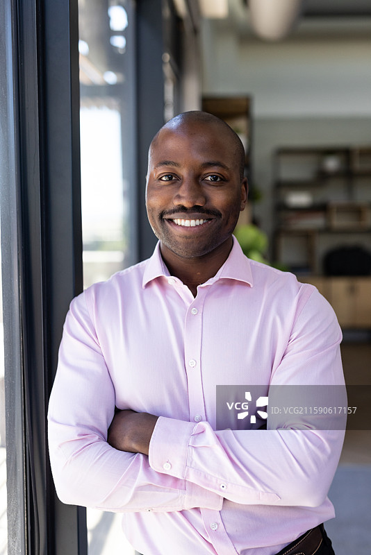 自信的商人在办公室窗边穿着粉色衬衫，温暖地微笑图片素材