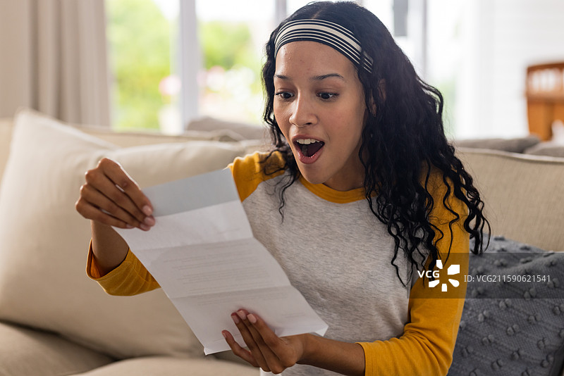 兴奋的女人坐在沙发上阅读信件，惊讶和快乐地在家中表达情感图片素材