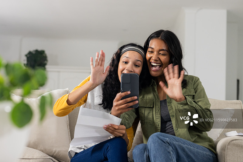 微笑的女性在舒适的客厅沙发上通过智能手机进行视频通话并挥手。图片素材