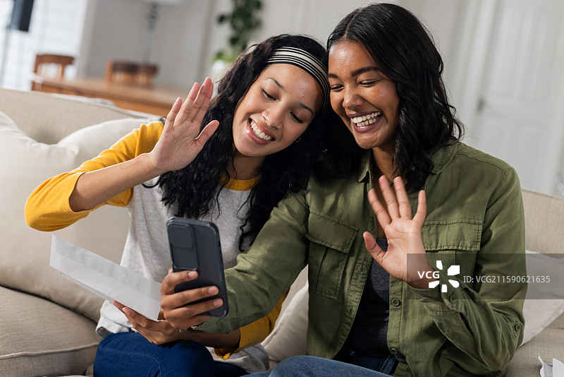 母女在家用智能手机视频聊天，微笑并挥手。图片素材