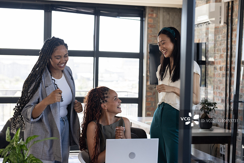 庆祝成功，同事们在现代办公室围绕笔记本电脑，分享快乐图片素材