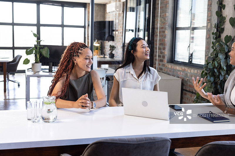 非裔美国女性和亚洲女性在办公室会议中微笑并讨论想法图片素材