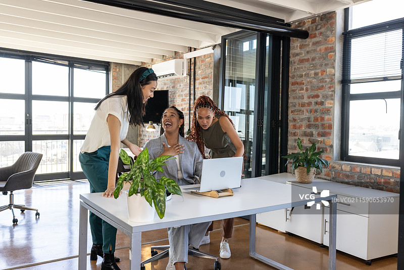 同事们在办公室庆祝成功，微笑着看着笔记本电脑屏幕。图片素材