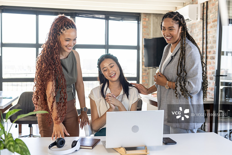 庆祝成功，同事们在办公室围着笔记本电脑微笑并合作图片素材