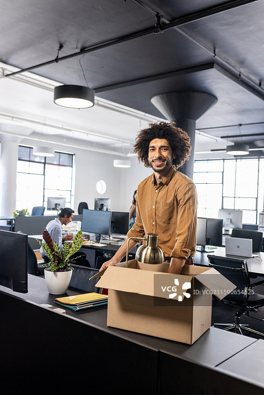 微笑的男子在现代办公室桌子上拆箱，开始新工作图片素材
