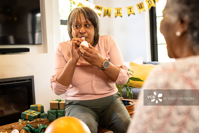 女人在生日派对上快乐地咬着杯子蛋糕，周围有礼物和装饰。图片素材