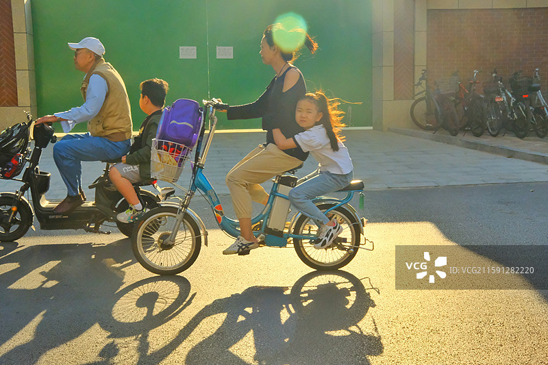 清晨明媚阳光中，送孩子们上学的家长们。城市生活。红领巾学生光影图片素材