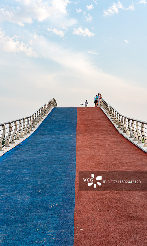河北衡水湖湿地公园在多云的天空中行走在桥上的人的后视图图片素材