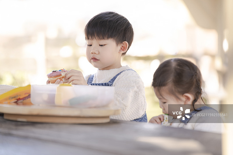 坐在野外露天餐桌享受西点美食的男孩女孩图片素材