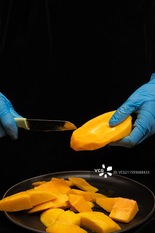 戴着蓝色手套的手正在切芒果图片素材