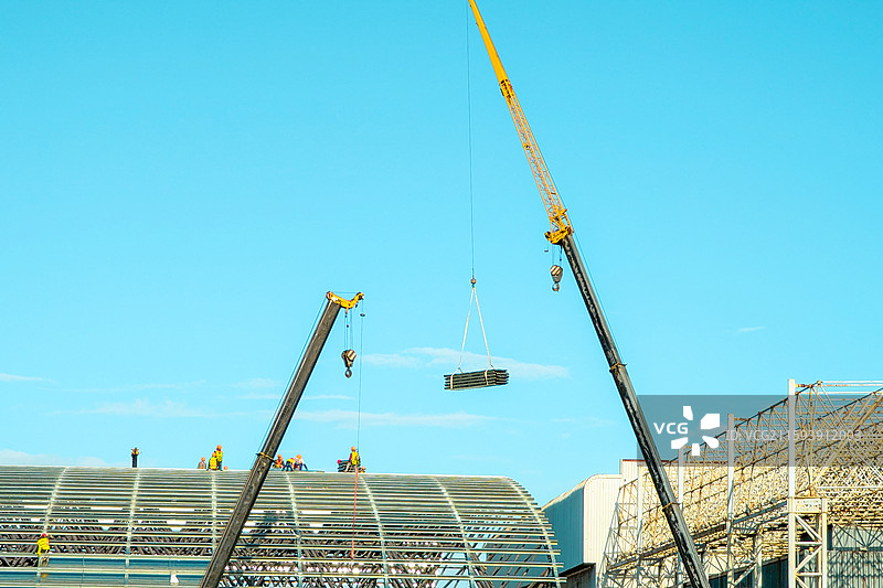 蓝天下屋顶上的建筑工人与起重机图片素材