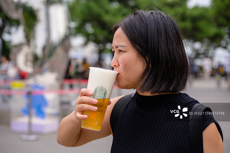 一名年轻亚洲女人在街上喝啤酒图片素材