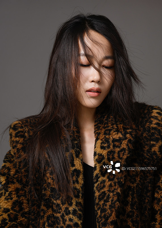 灰色背景下身穿豹纹大衣的年轻女子肖像图片素材