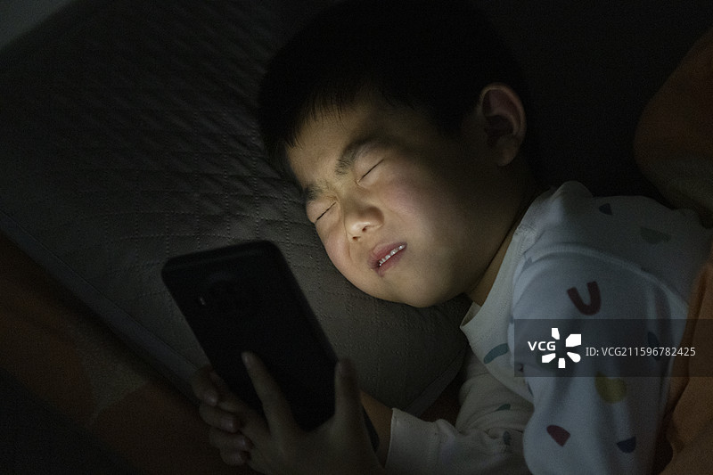 小朋友夜晚躺床看手机图片素材