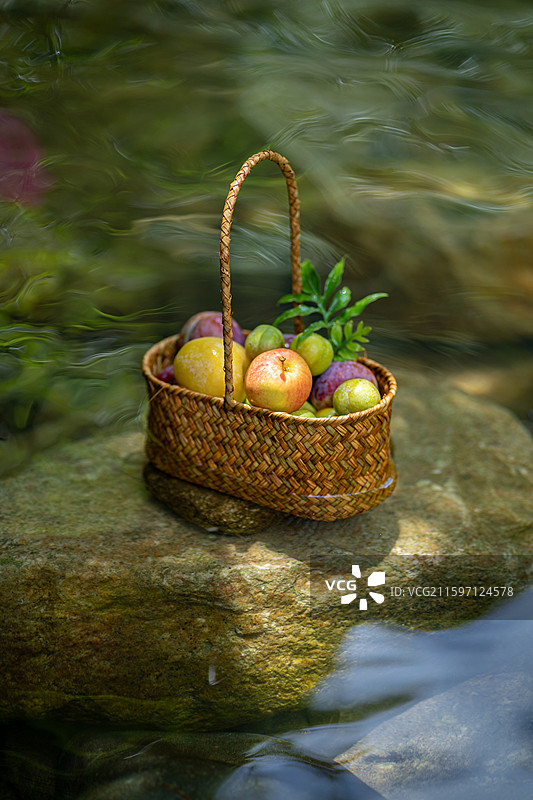 溪流中石头上摆放的新鲜水果果篮图片素材