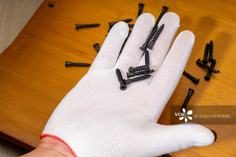 戴着白色手套的手掌中拿着黑色螺丝图片素材