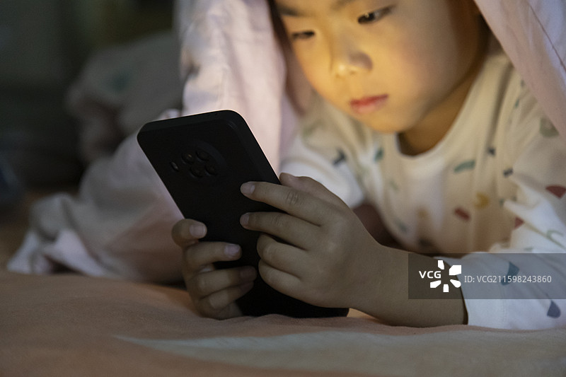 小朋友夜晚躺床看手机图片素材