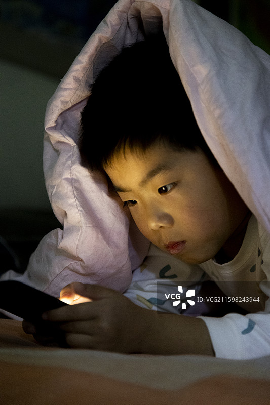 小朋友夜晚躺床看手机图片素材