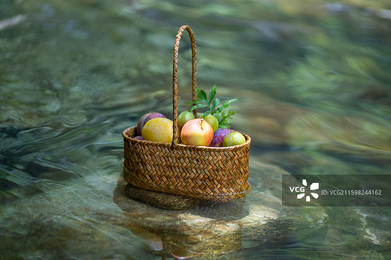 溪流中石头上摆放的新鲜水果果篮图片素材