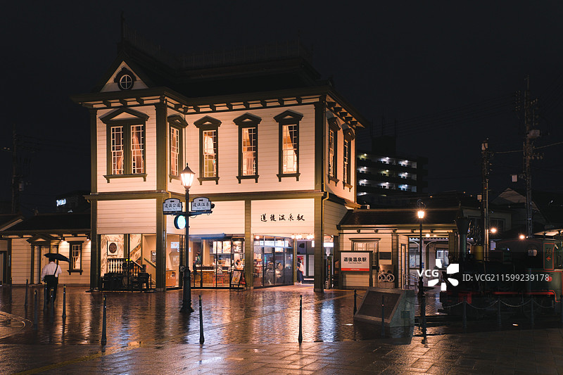 日本爱媛县松山市道后温泉站，雨后夜晚的路面有轨电车车站图片素材