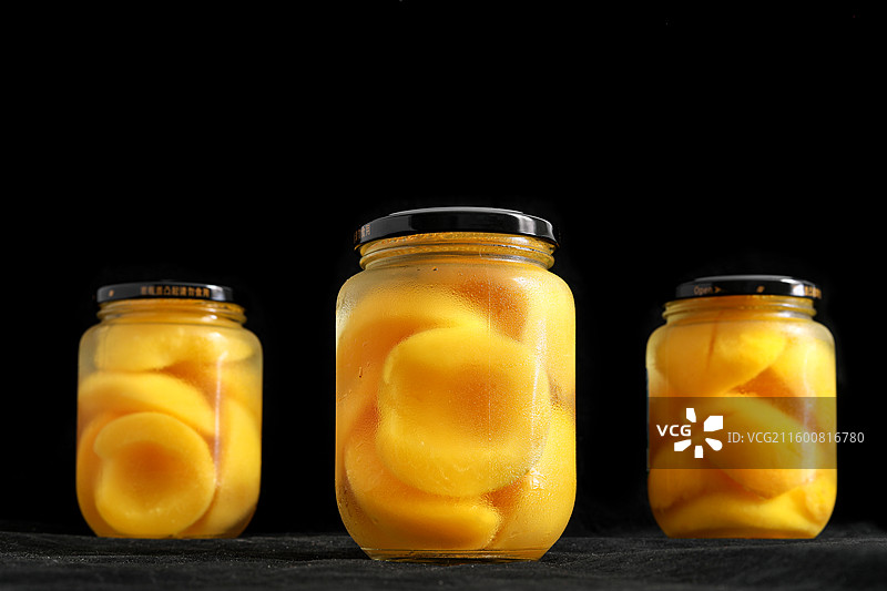 黑色背景上的一玻璃瓶童年美食零食黄桃罐头特写图片素材